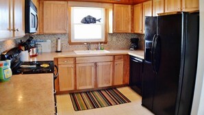 Une cuisine avec des meubles en bois, un réfrigérateur noir, une cuisinière et une fenêtre décorée avec un motif de poisson.