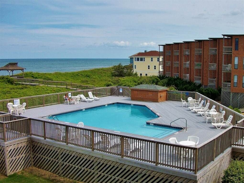 Una piscina en la azotea con sillones de descanso y una terraza de madera, con vista a una playa y al océano.
