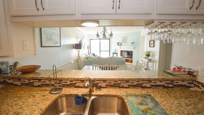 A kitchen with a double sink, a backsplash with mosaic tiles, and a dining area visible through an open doorway. - Great condo in Duck, NC (Duck)