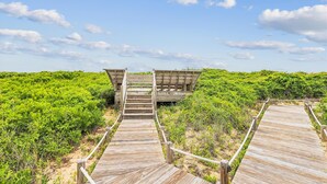 A wooden boardwalk leading to a structure with a sloped roof, surrounded by dense green vegetation. - Great condo in Duck, NC (Duck)
