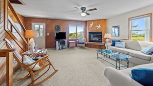 A spacious living room with a ceiling fan, wooden walls, a large window, and a television.