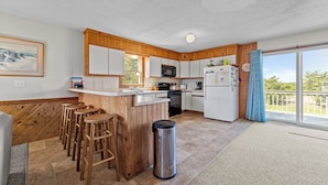 A kitchen with wooden cabinets, a microwave, a refrigerator, and a bar area with stools.