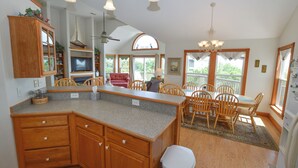 A spacious kitchen with wooden cabinets, a granite countertop, and a dining area with wooden chairs and a table. - Enjoy ocean views from this beautiful home, nestled in a quiet soundside community. (Nags Head)