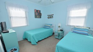 A bedroom with two beds, a desk, a chair, and a window with blinds. - Pet Friendly on Outer Banks. (Kill Devil Hills)