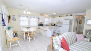 A compact kitchen with white cabinetry, a dining table with chairs, and a striped sofa. - Pet Friendly on Outer Banks. (Kill Devil Hills)
