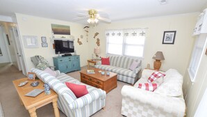 A living room with striped sofas, a wooden coffee table, and a television. - Pet Friendly on Outer Banks. (Kill Devil Hills)