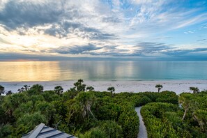 A coastal view with a beach, dense greenery, and a clear sky.