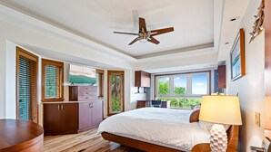 A modern bedroom with a large bed, wooden flooring, a ceiling fan, and a view of greenery outside. - Stella Marris- N. Captiva Island | Luxury Beachfront Retreat (Lee County)