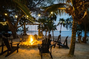 A beachside seating area with chairs, a fire pit, and string lights. - Shedrock Shangrila, Beachfront Pelican Penthouse Suite (Hopkins)