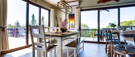 A spacious dining area with a wooden table and chairs, large windows with curtains, and a view of the outdoors.