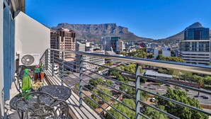 A balcony with a table, a Samsung air conditioner, and a view of a cityscape with buildings and a mountain in the background. - Quayside 1206by CTHA (Cape Town)