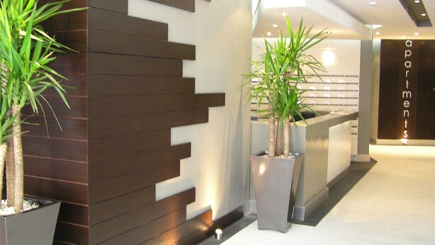 A modern reception area with a wooden accent wall, two potted plants, and a reception desk labeled "apartments". - Quayside 1206by CTHA (Cape Town)