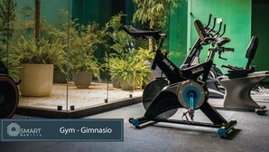 Un vélo d’appartement dans une salle de sport, avec un mur vert et des plantes en pot.