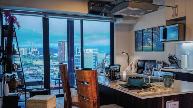 Une cuisine moderne avec vue sur la ville, un coin repas offrant également une vue panoramique, et une grande fenêtre.