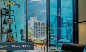 A modern living room with a large window offering a city view, a bookshelf, and a comfortable seating area.