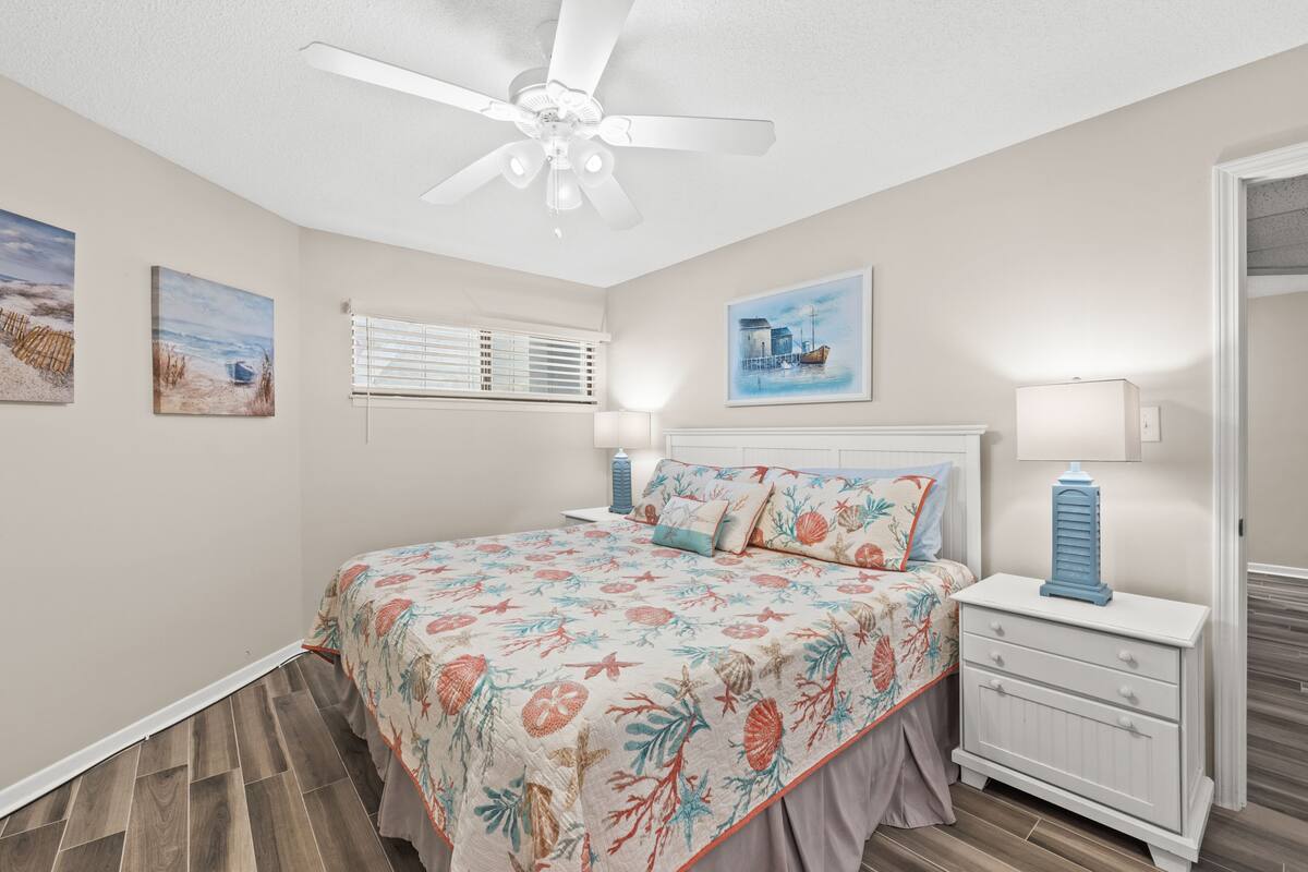 A bedroom with a bed, a nightstand, a ceiling fan, and wall art.
