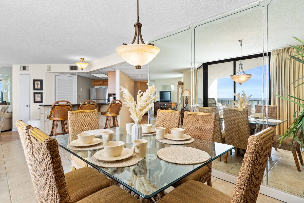 A dining area with a glass table, wicker chairs, and a view of the ocean.