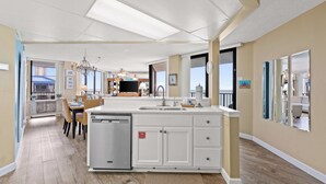 A spacious kitchen with a dishwasher, a dining area with chairs, and a large window. - AquaVista by Book That Condo (Panama City Beach)