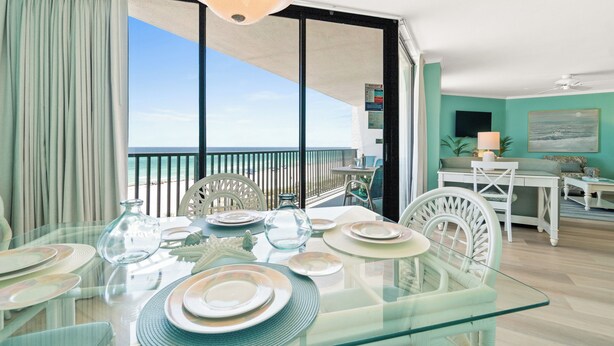 A dining area with a glass table, white chairs, and a view of the ocean. - AquaVista by Book That Condo (Panama City Beach)