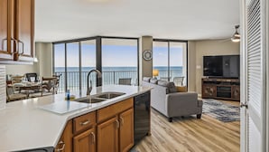 A modern kitchen with a large island, a dining area with a view, a living room with a TV, and a balcony with a view. - AquaVista by Book That Condo (Panama City Beach)