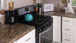 Een keuken met witte kastjes, een fornuis, een magnetron en een koffiezetapparaat.