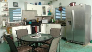 Een compacte keuken met witte kastjes, een roestvrijstalen koelkast, een magnetron en een eettafel met stoelen.