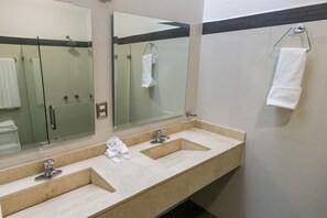 A bathroom with two sinks, a glass shower enclosure, and a towel rack. - La Loma Suites (Ixtapa)