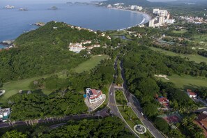 An aerial view of a coastal resort with a golf course, a road, and buildings. - La Loma Suites (Ixtapa)