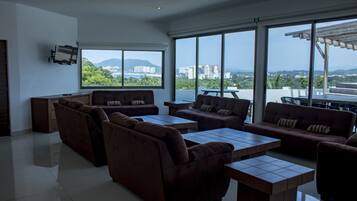 Una sala de estar moderna con sofás, una mesa de centro, ventanas amplias con vistas a la ciudad y un televisor de pantalla plana montado en la pared.