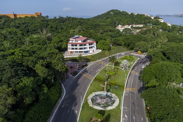 A multi-story building with a red roof, surrounded by lush greenery and a winding road. - La Loma Suites (Ixtapa)