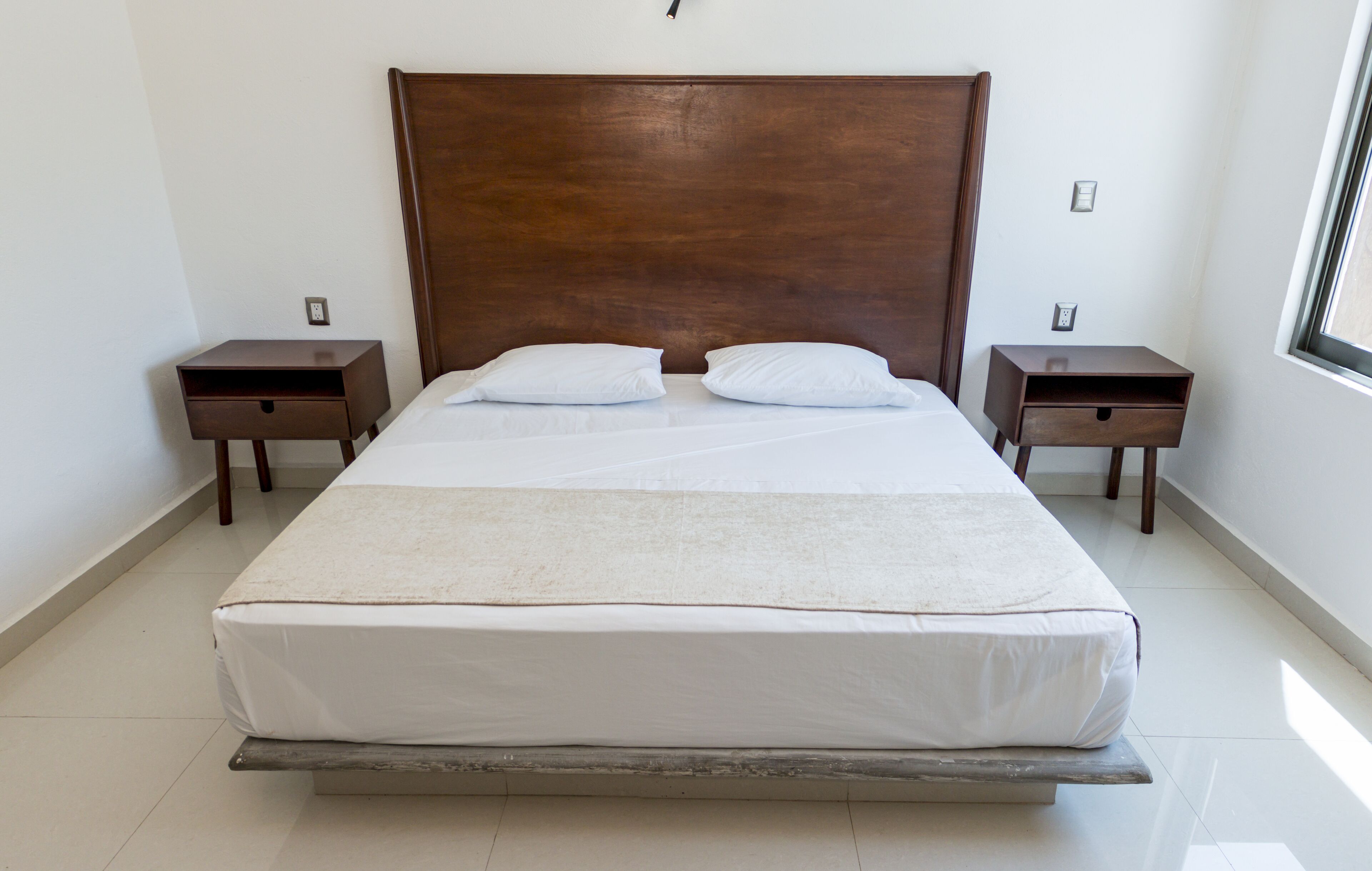 A large bed with a wooden headboard, two nightstands, and a window on the right.