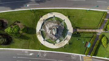 Vista aerea di una rotonda con fontana al centro, circondata da prati verdi e alcuni alberi.