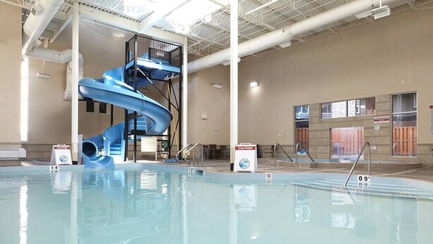 An indoor swimming pool with a blue water slide and a caution sign. - Beautiful 2 Bed 2 bath Pool Waterslide & Hot tubs (Canmore)