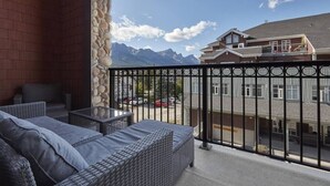 A balcony with wicker furniture, a stone wall, and a view of a building and mountains. - Beautiful 2 Bed 2 bath Pool Waterslide & Hot tubs (Canmore)