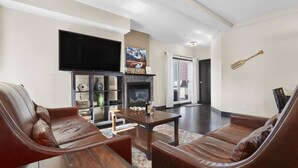 A modern living room with leather sofas, a wooden coffee table, a flat-screen TV, a fireplace, and a large window. - Beautiful 2 Bed 2 bath Pool Waterslide & Hot tubs (Canmore)