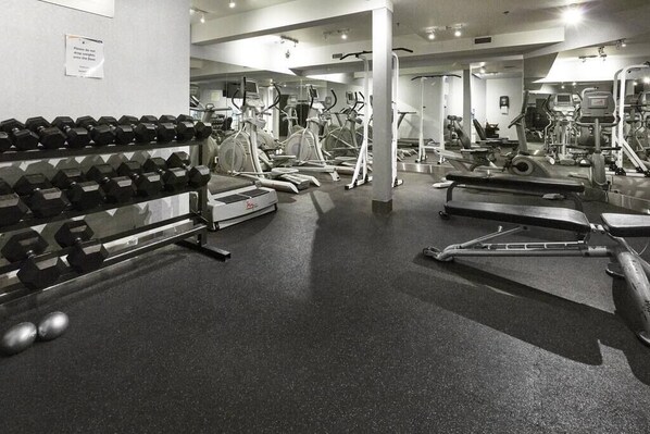 Un gimnasio con varios equipos de ejercicio, incluyendo cintas de correr, elípticas y pesas libres.