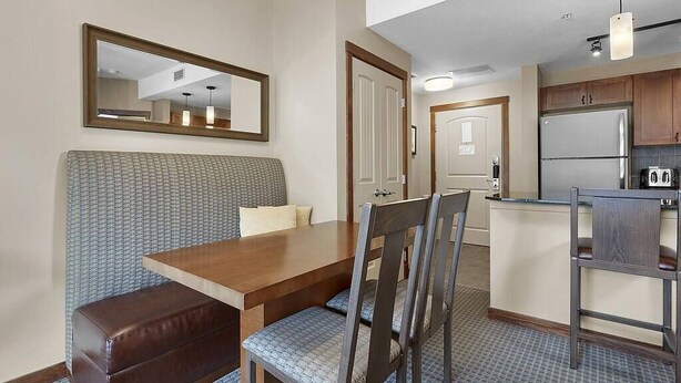 A compact hotel room with a kitchenette, a dining area with a bench and chairs, and a large mirror on the wall. - Beautiful Mtn Views-King Bed, Hot Tub (Canmore)