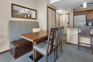 Ein kompaktes Hotelzimmer mit Küchenzeile, einem Essbereich mit einer Bank und Stühlen sowie einem großen Spiegel an der Wand.