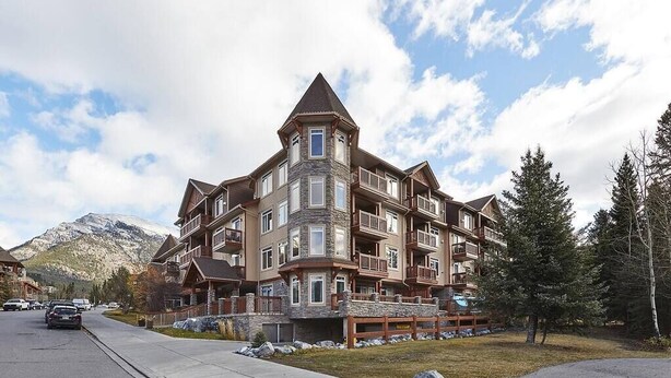 A multi-story hotel with a stone facade, multiple balconies, and a mountain backdrop. - Beautiful Mtn Views-King Bed, Hot Tub (Canmore)