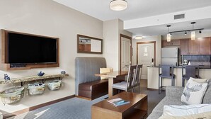 A modern living room with a flat-screen TV, a sofa, a coffee table, and a kitchen area in the background. - Beautiful Mtn Views-King Bed, Hot Tub (Canmore)