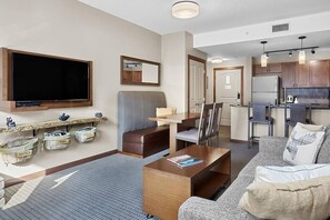 A modern living room with a flat-screen TV, a sofa, a coffee table, and a kitchen area in the background.