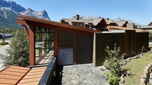 Een modern gebouw met grote ramen, een oprit van natuursteen en uitzicht op bergen.