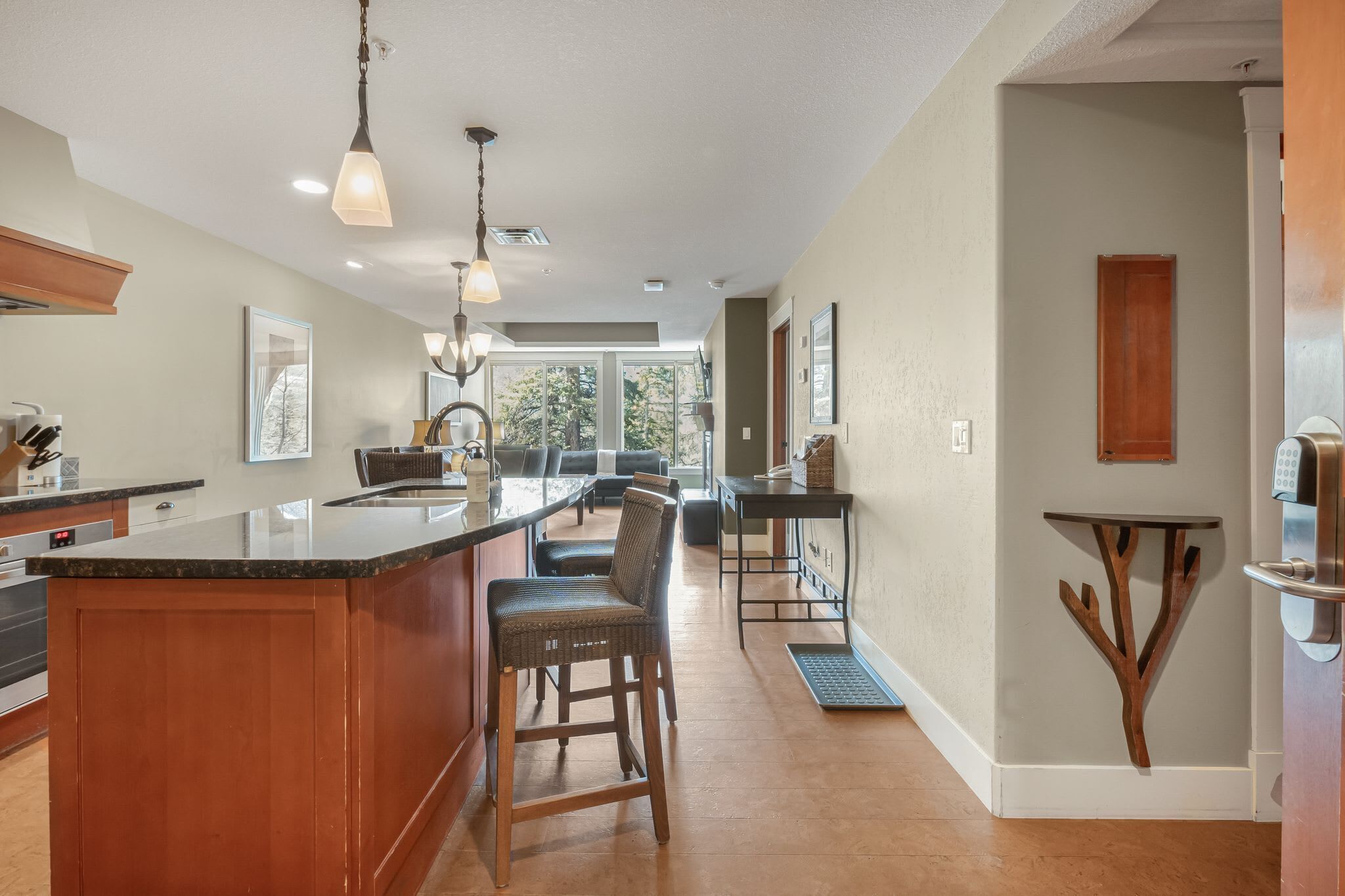 A modern kitchen with a central island, wooden chairs, pendant lighting, and a view to the outdoors.