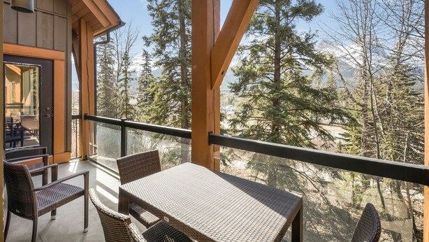 A balcony with wicker furniture, a glass railing, and a view of trees and mountains. - Star Suite 2 Bed 2 bath condo with 3 fireplaces (Canmore)