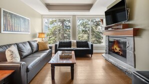 A living room with a fireplace, a sofa, a coffee table, and a TV. - Star Suite 2 Bed 2 bath condo with 3 fireplaces (Canmore)