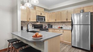 Een moderne keuken met lichte houten kastjes, een roestvrijstalen koelkast, een inbouwmagnetron en een centraal eiland met krukken.
