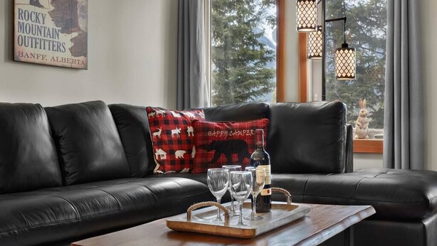 Een moderne woonkamer met een leren bank, een houten salontafel met wijnglazen en een fles, en een raam met uitzicht op bomen.