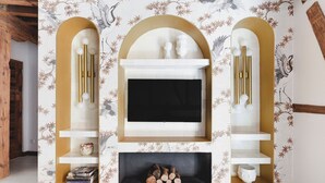 A modern living room with a fireplace, wooden beams, and a decorative wall with floral patterns. - ~TROPIC~ by myhomeintoledo.com (Toledo)
