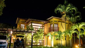 Un edificio de dos pisos con fachada amarilla, un área de estacionamiento techada y varias palmeras.