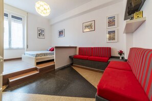 A compact living space with a bed, a sofa, a small table, and a staircase.